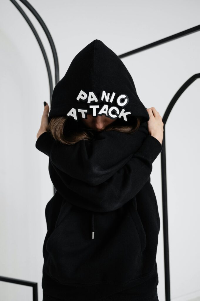 Young woman with hood up, text 'panic attack' visible, emphasizing mental health.