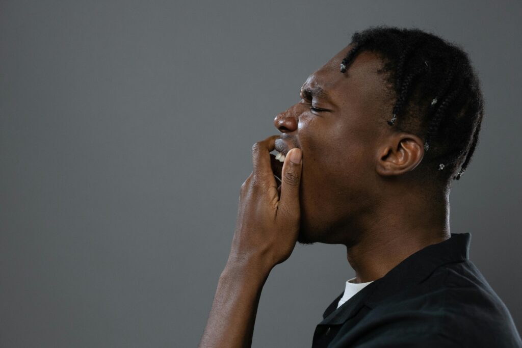 Close-up side view of a black man yawning against a neutral background. Minimalist and candid.