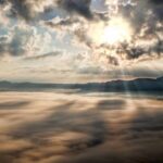 Captivating view of the sun breaking through clouds over a mist-covered mountain range.