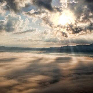 Captivating view of the sun breaking through clouds over a mist-covered mountain range.